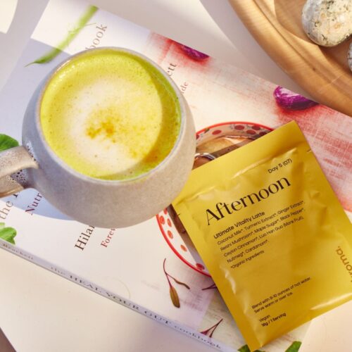 Kroma Vitality Latte sachet on top of a book next to a yellow tumeric latte frothed. All resting on a table