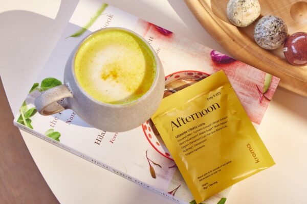 Kroma Vitality Latte sachet on top of a book next to a yellow tumeric latte frothed. All resting on a table