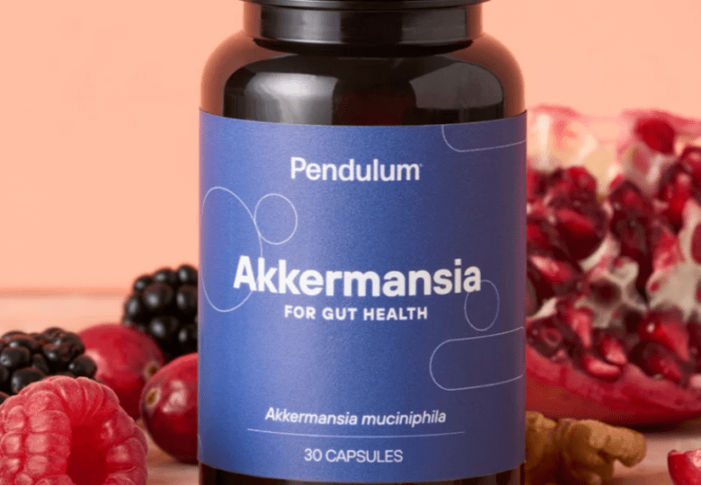 Black Akkermansia bottle with 30 capsules affixed with a blue label and a pink background with raspberries blackberries and walnuts