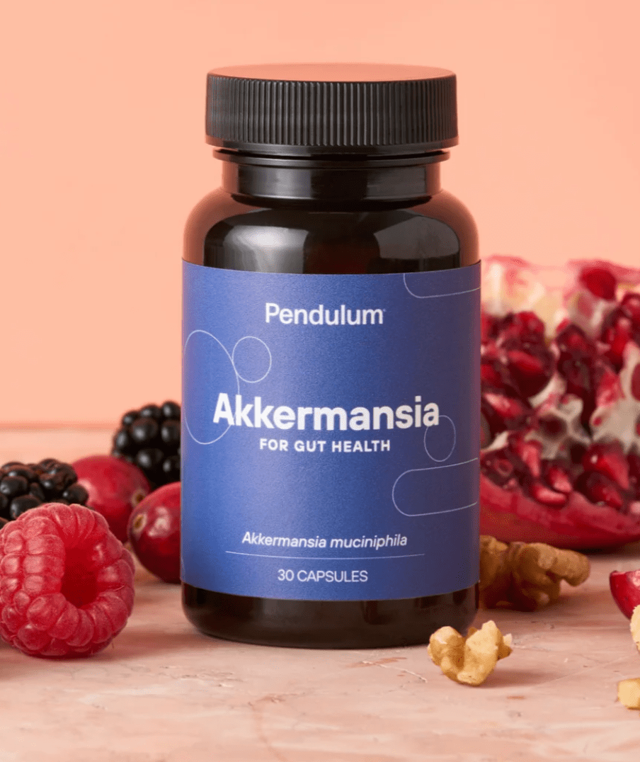Black Akkermansia bottle with 30 capsules affixed with a blue label and a pink background with raspberries blackberries and walnuts
